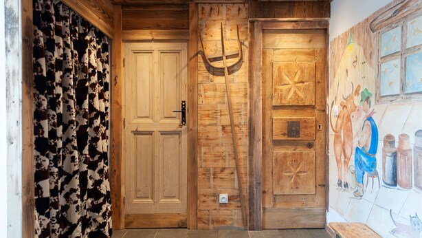 A wooden interior with a cow-patterned curtain, a door, and a mural of a cow and a person. - Chalet Marcel et Grégoire (Les Belleville)