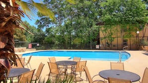 A swimming pool with lounge chairs and tables, surrounded by trees and a building.