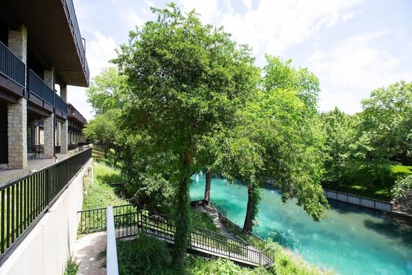 A building with a balcony overlooking a river, surrounded by greenery.