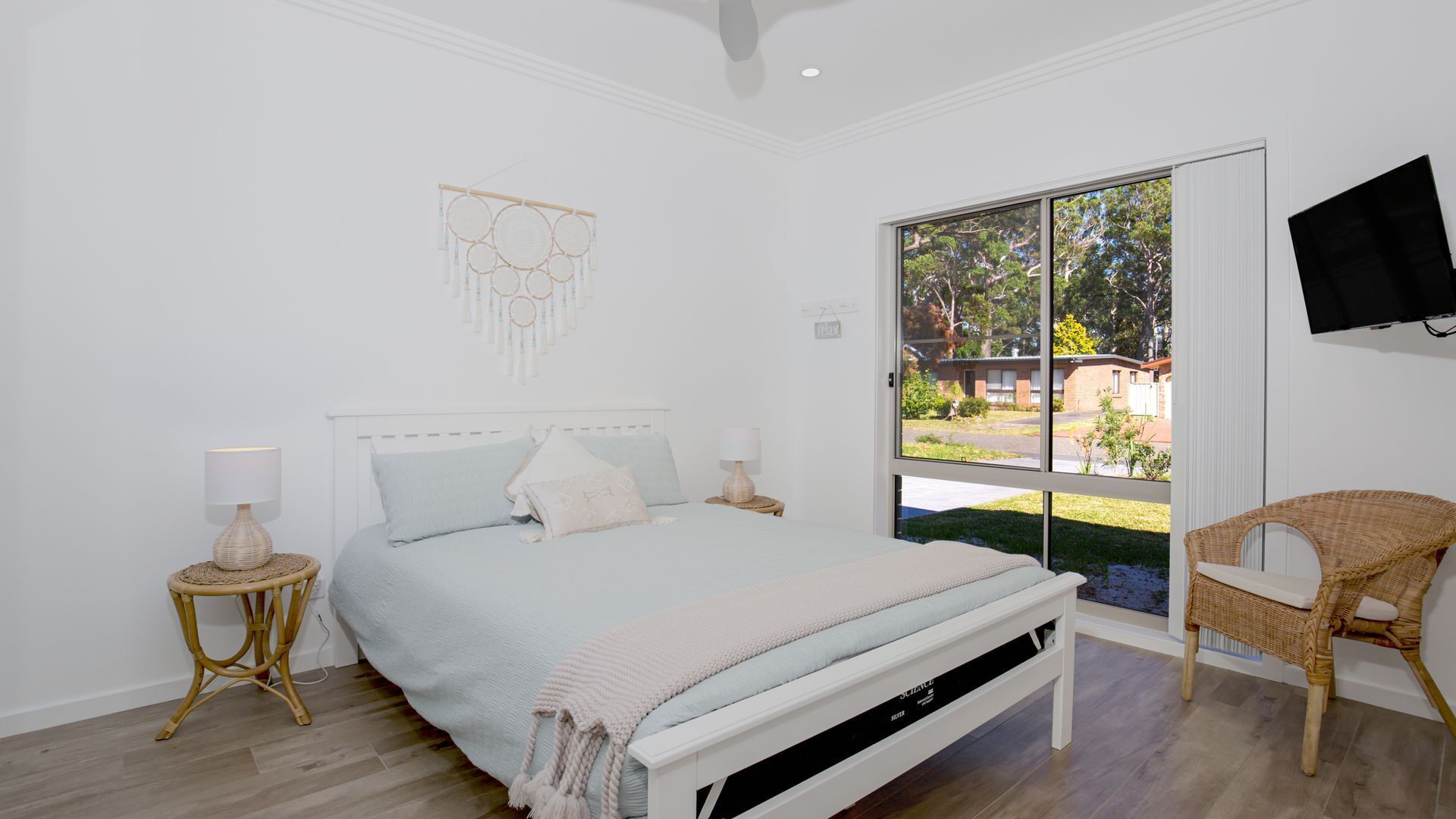 A bedroom with a bed, bedside tables, a chair, a TV, and a view of the outside.