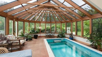 A conservatory with a pool, wooden beams, and potted plants.