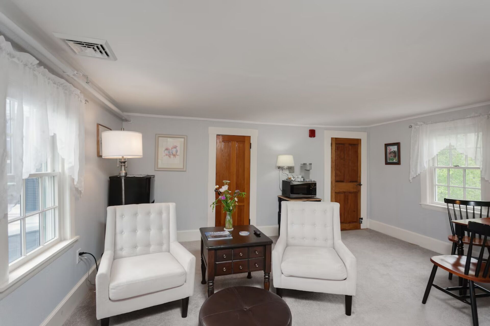 A living room with two white armchairs, a small table with a vase, a television, and a wooden door.