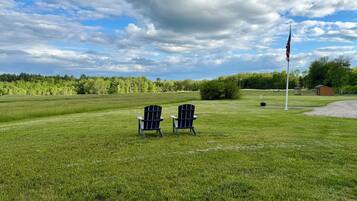 A grassy field with two Adirondack chairs and a flagpole.