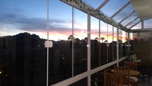 A room with a large window overlooking a cityscape at sunset.