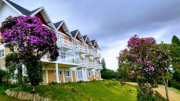 A multi-story hotel with balconies, surrounded by lush greenery and flowering trees.