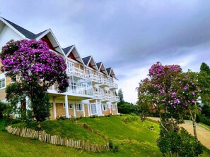 Un hôtel à plusieurs étages, doté de balcons, entouré d’une végétation luxuriante et d’arbres en fleurs.