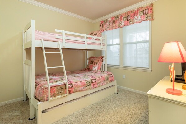 A bunk bed with a ladder, a desk with a lamp, and a window with curtains.