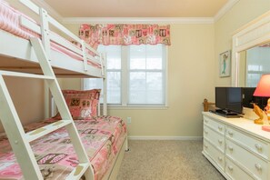 Un dormitorio con literas, cómoda, televisor y ventana con adornos decorativos.
