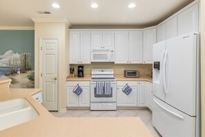 Una cocina con armarios blancos, microondas, horno, refrigerador y una encimera con cafetera.