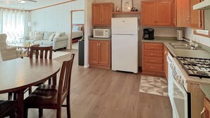 A spacious kitchen with wooden cabinets, a refrigerator, stove, and a dining area with a table and chairs. - Riverside Cottage w/ 70' Private Dock - 5 Minutes From Town! (Cheboygan)