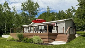 A modern cabin with a deck, outdoor seating, and a red umbrella. - Riverside Cottage w/ 70' Private Dock - 5 Minutes From Town! (Cheboygan)