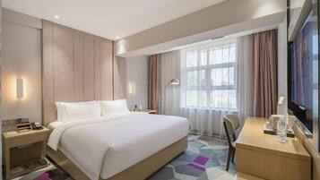 Habitación de hotel con una cama grande, mesitas de noche, un escritorio, una silla, un televisor y una ventana con cortinas.