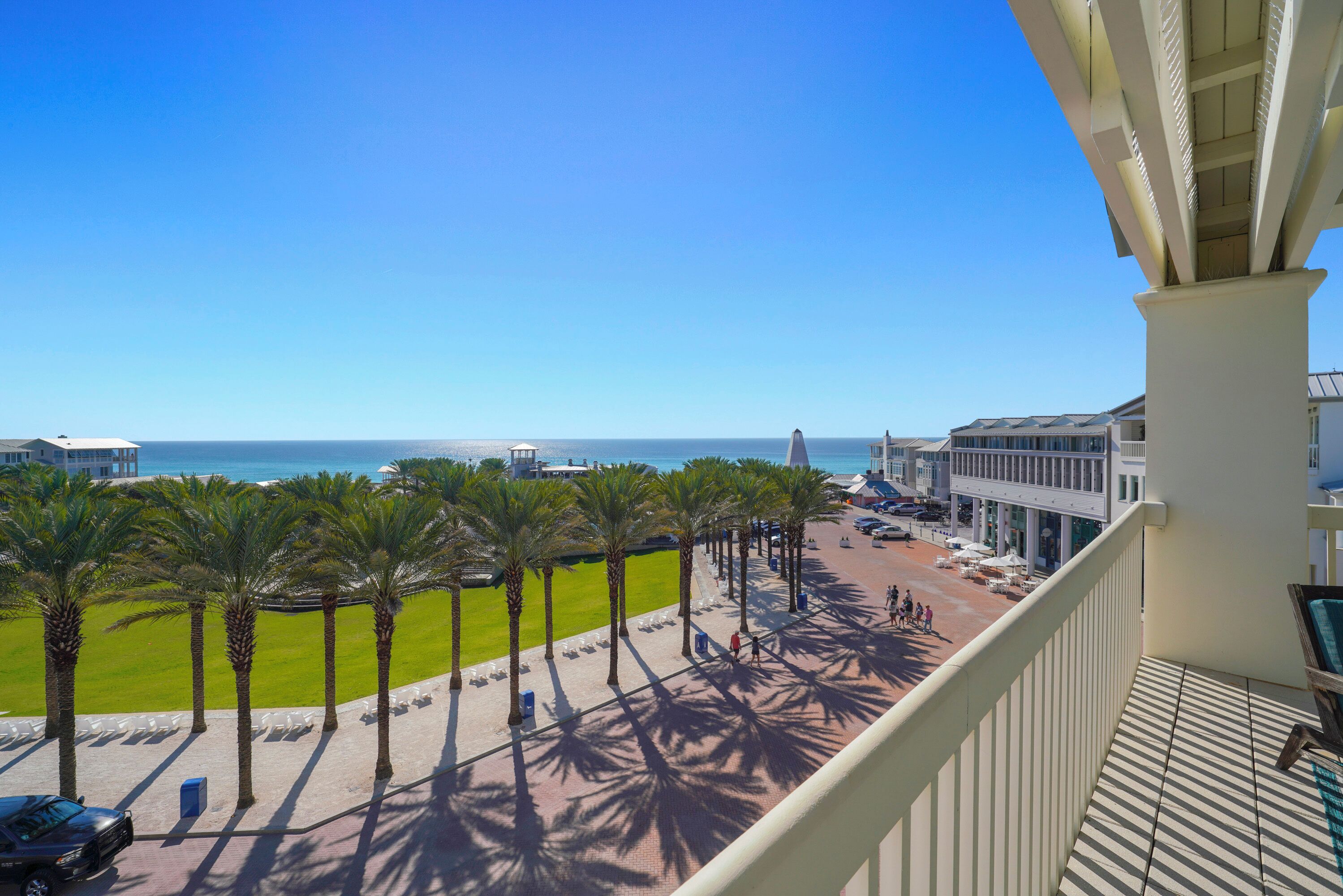 A balcony with a view of a beach, palm trees, and a clear blue sky.