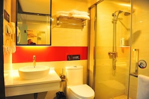 A bathroom with a sink, toilet, and shower. There is a mirror above the sink and a towel rack. The walls are tiled, and there is a sign indicating a 'slippery floor' warning.
