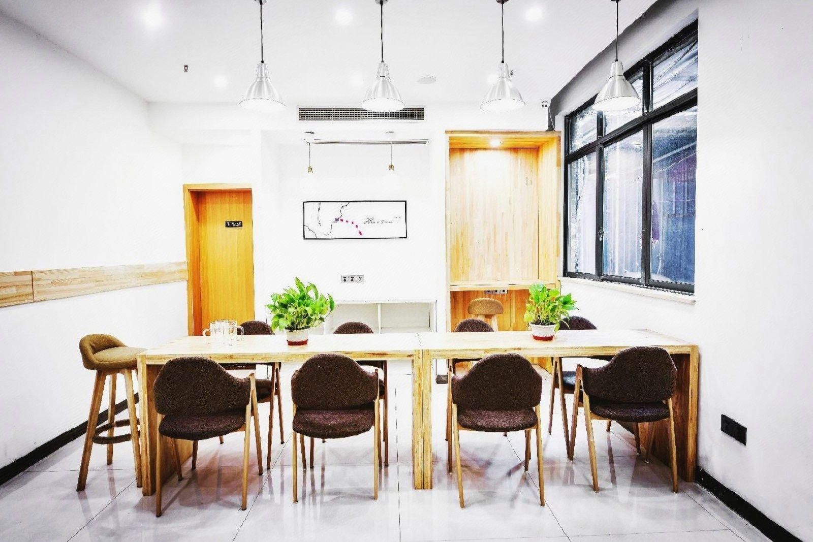 A conference room with a long table, four chairs, two potted plants, pendant lighting, a map on the wall, and a window with a view.