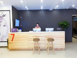 A reception desk with a number sign, a digital screen, and two stools.