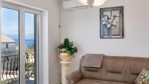 A living room with a sofa, a potted plant, and a painting on the wall.