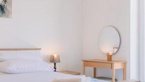 A neatly made bed with white linens, a bedside lamp, a wooden nightstand, and a round mirror on the wall.