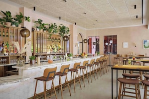 Eine Bar mit einer langen Theke, mehreren Hockstühlen und Regalen mit Flaschen und Pflanzen.
