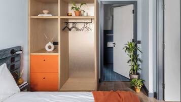 Un dormitorio con una cama, un armario, una mesita con un florero y una planta en maceta.