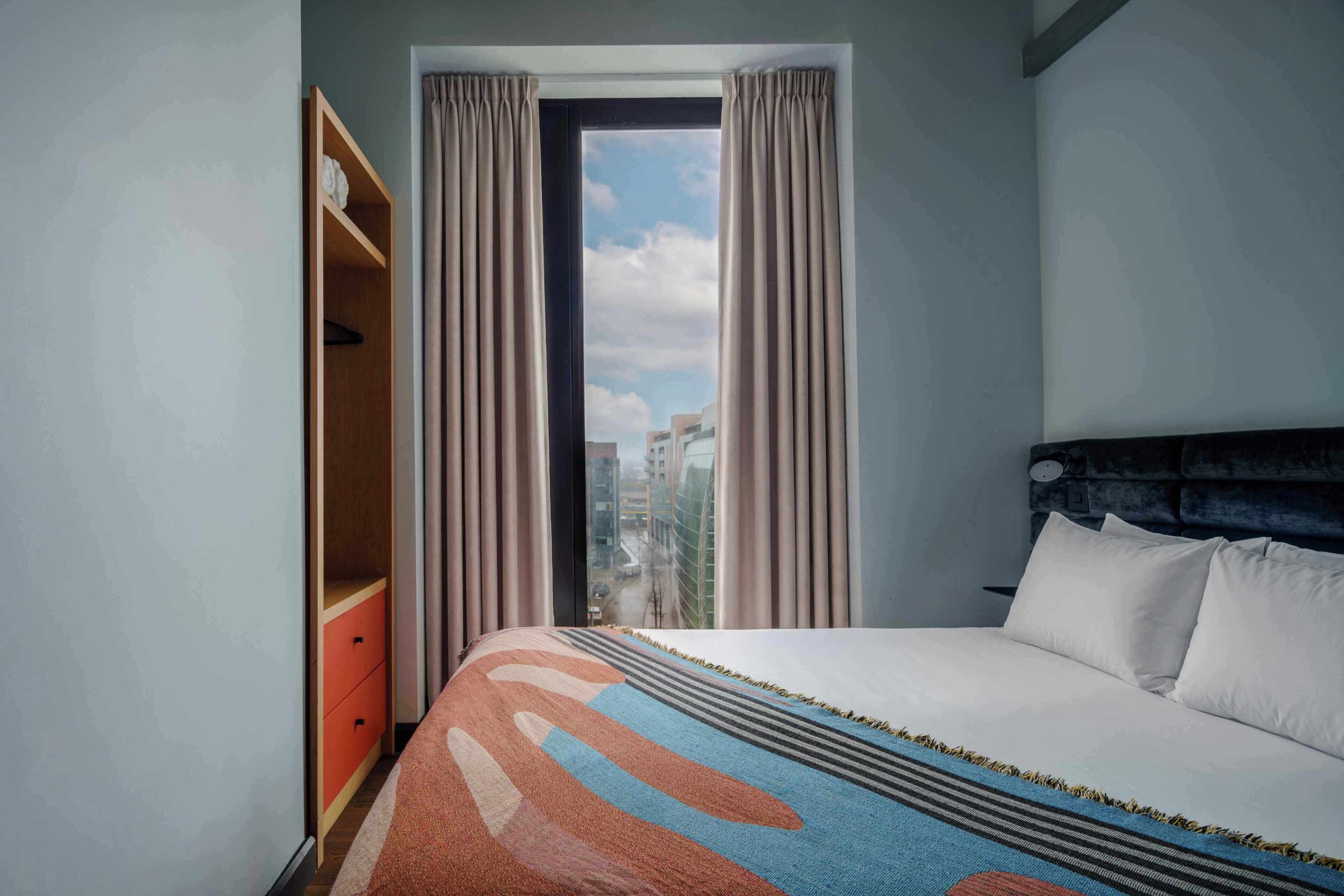 Una habitación de hotel con cama, armario y ventana con cortinas.