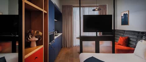 A hotel room with a bed, a desk with a TV, a wardrobe, and a window with curtains.