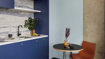 Une cuisine avec des meubles de couleur bleue, un pare-feu en marbre, un évier, une plante en pot, un vase contenant des plantes séchées et une table ronde avec une chaise.
