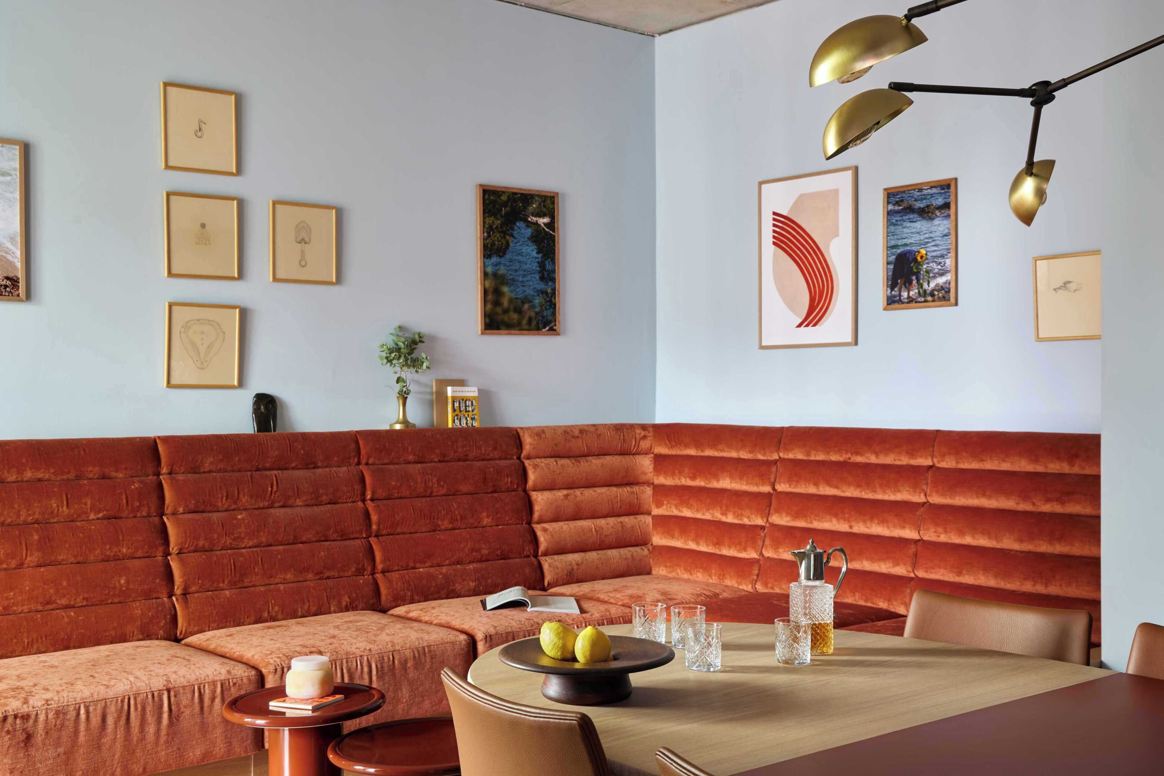 A modern interior with a red cushioned bench, a round table with drinks, and framed artwork on the walls.