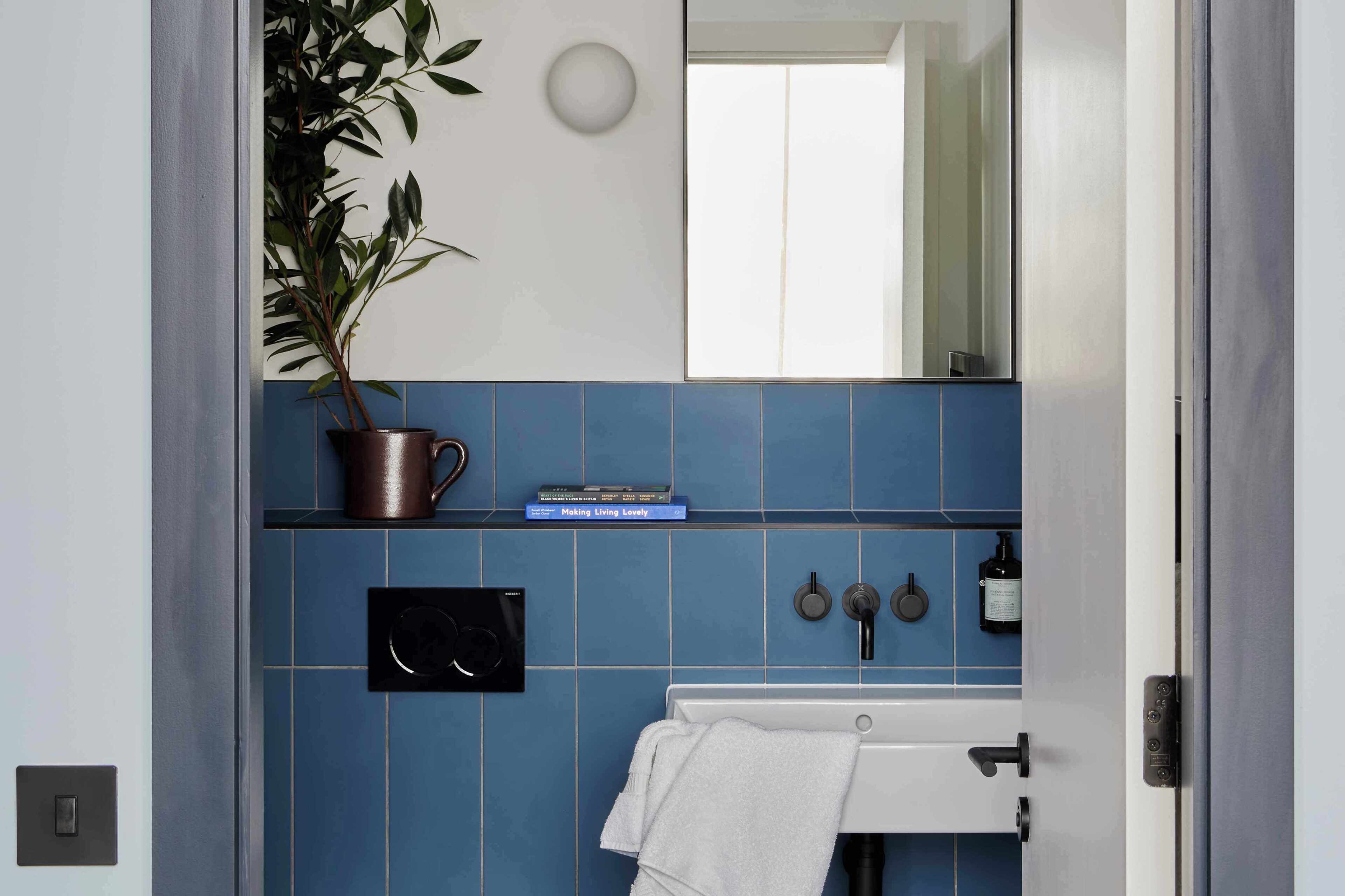 A bathroom with a blue tiled wall, a white sink, a towel, a potted plant, and a mirror.