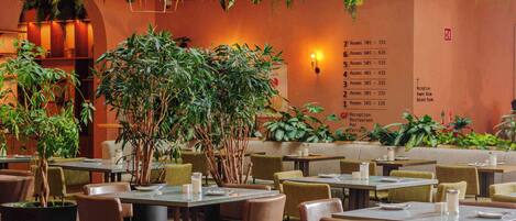 Un restaurant avec des tables et des chaises, un mur sur lequel figure une liste des numéros de chambre, et des plantes suspendues.