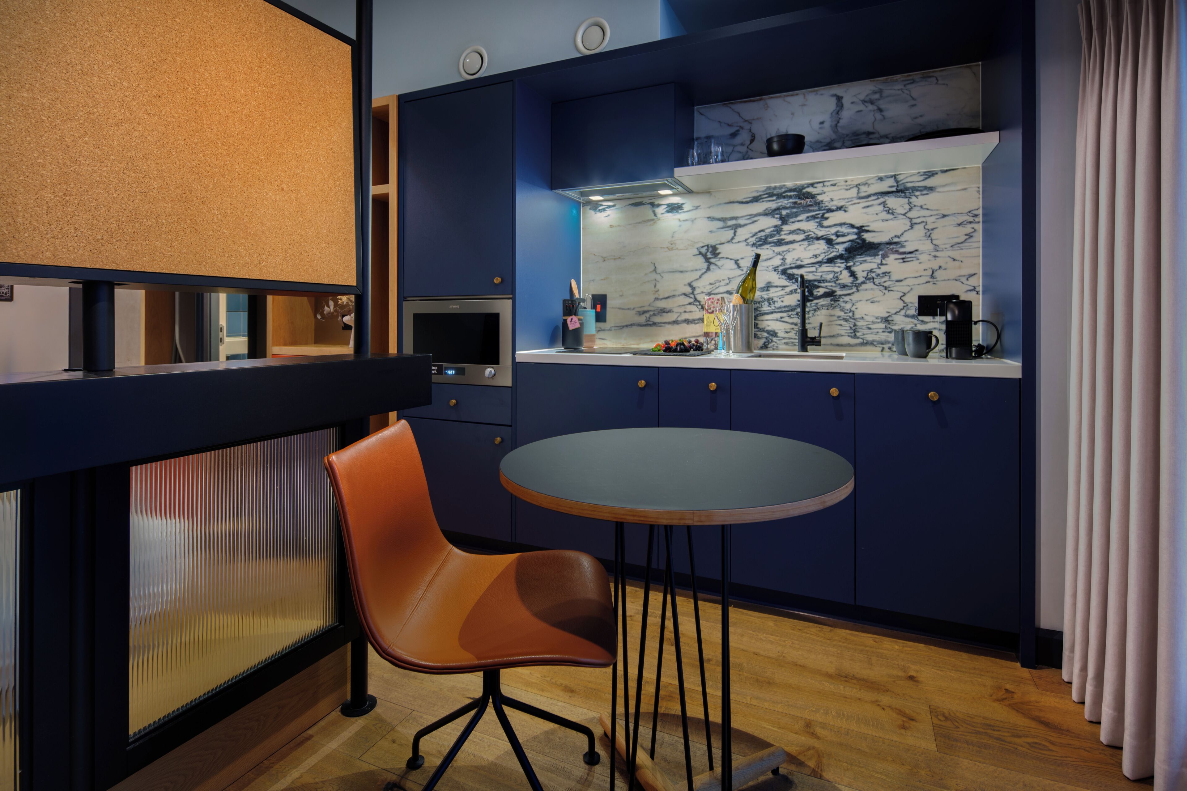 Een moderne keuken met een marmeren achterwand, een ronde tafel en een losse oranje stoel.