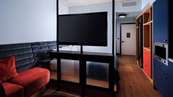 Quarto com televisão de tela plana em um suporte, sofá vermelho, piso de madeira e guarda-roupa com portas vermelhas e azuis.