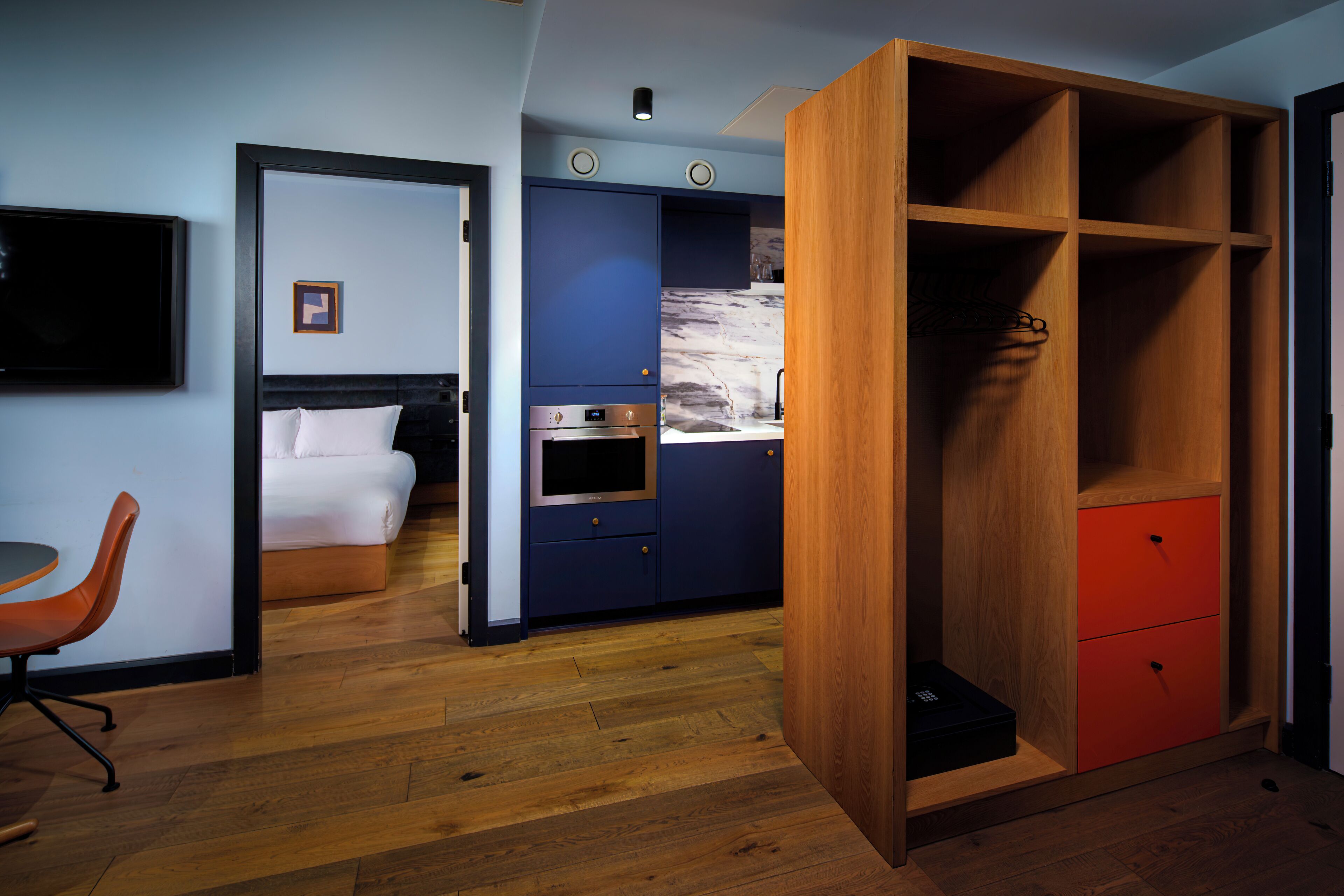 Una habitación de hotel con cama, escritorio, armario, zona de cocina y televisión.