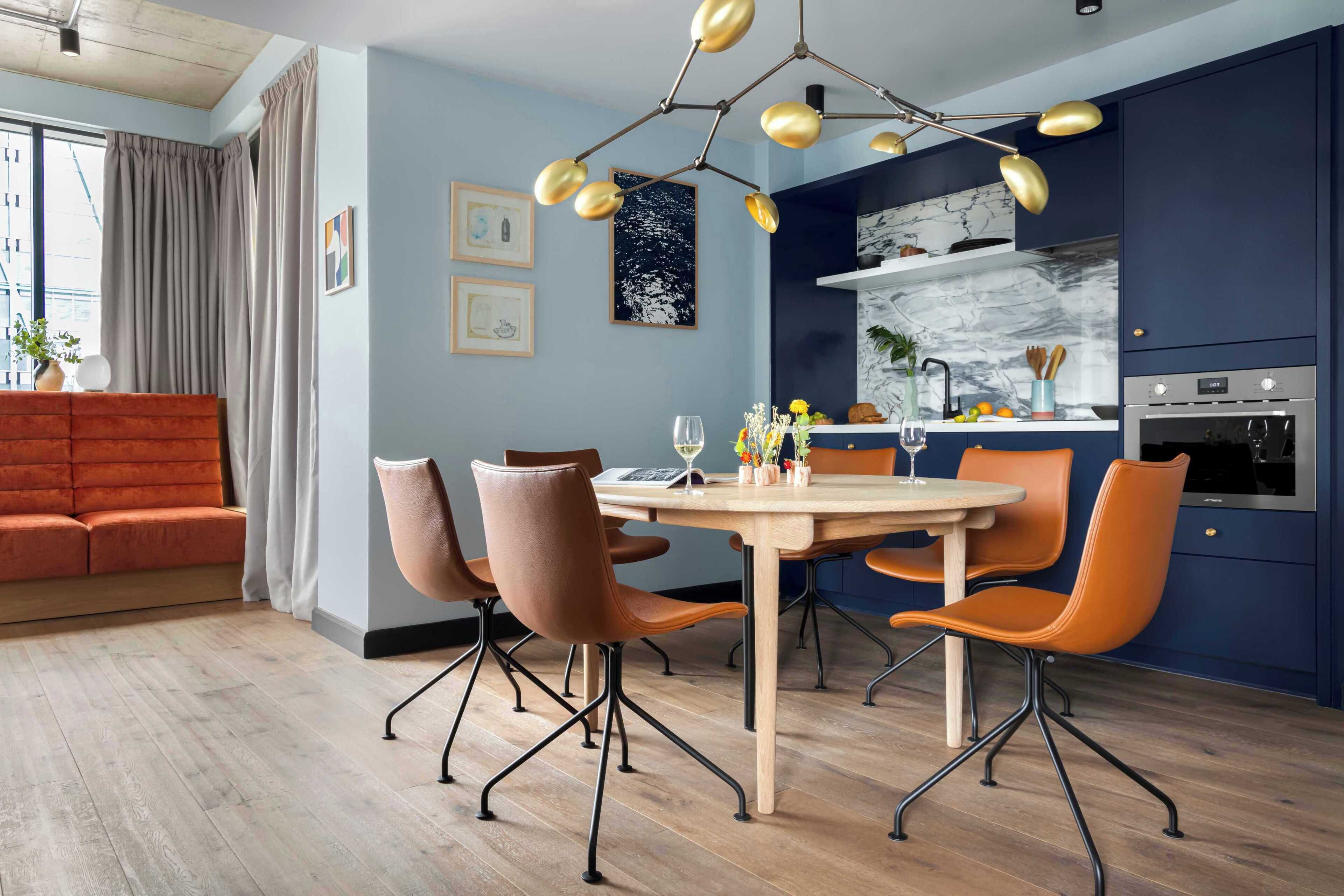 Una cocina moderna con comedor, que incluye una mesa redonda, sillas color naranja y un horno empotrado.
