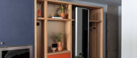 A room with a built-in oven, wooden shelving with plants, and a large mirror.
