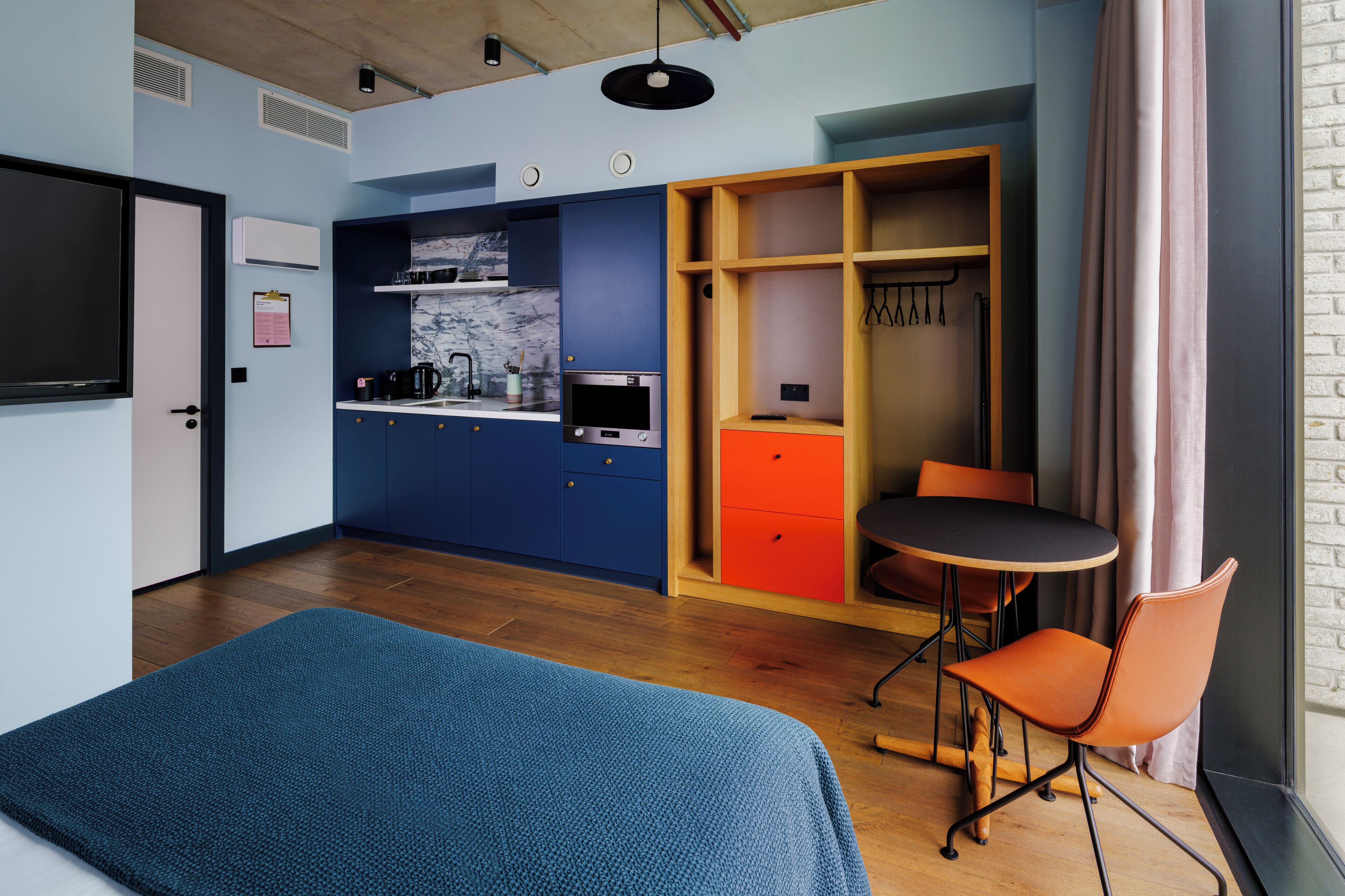 Une pièce compacte comprenant un lit, un coin cuisine, un espace repas et une armoire.