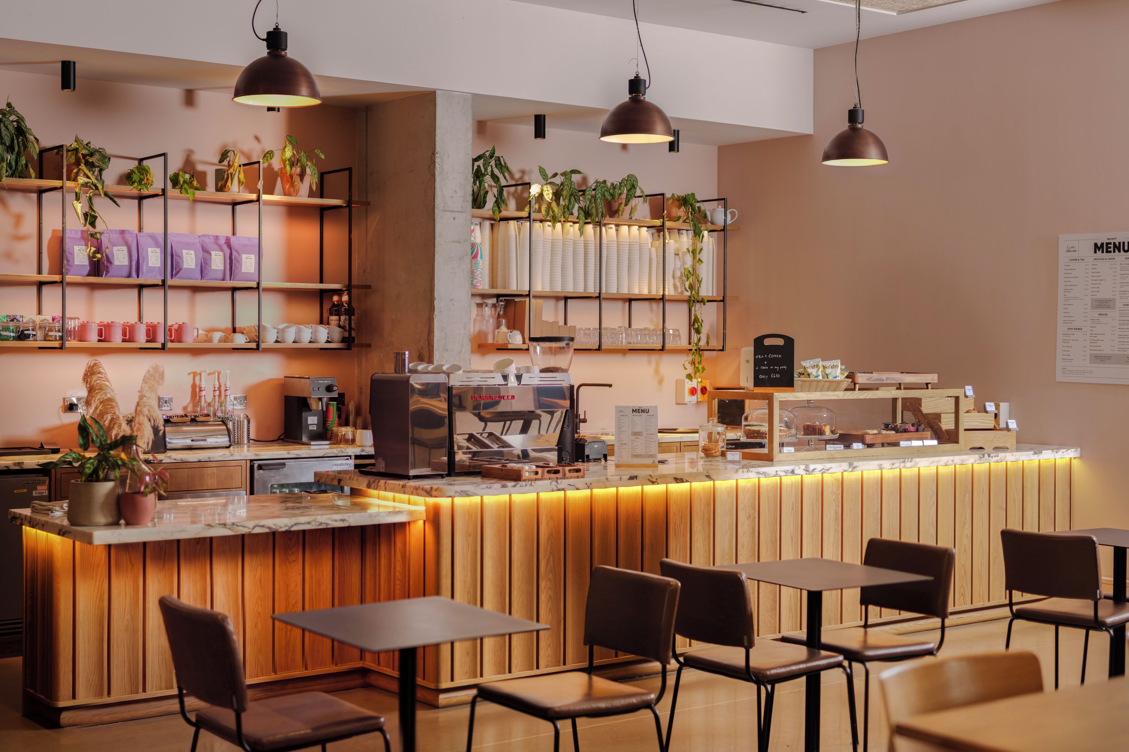 A cafe with a wooden counter, seating area, and shelves with plants and kitchen items.