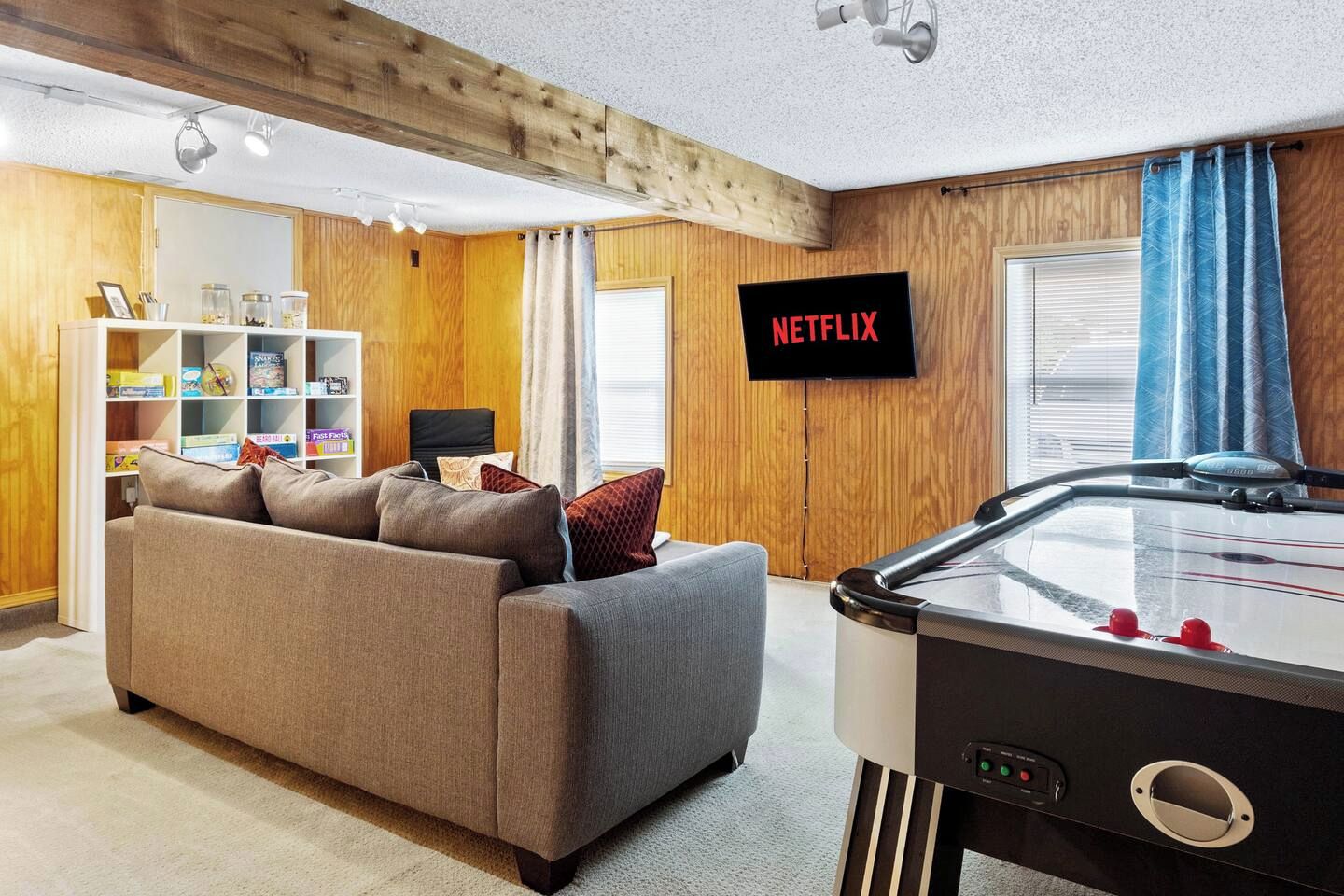 A cozy living room with a sofa, a pool table, a bookshelf, and a TV displaying 'NETFLIX'.