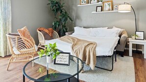 Quarto com cama, uma cadeira, mesa com planta e parede com quadros.
