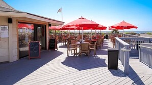 An outdoor deck with tables and red umbrellas, a sign indicating a men's restroom, and a view of the ocean. - KING BED Oceanview 1BR Top Floor Villa (Hilton Head Island)