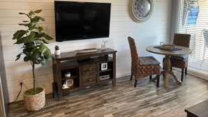 A living room with a flat-screen TV, a round table with chairs, a potted plant, and a wall clock. - KING BED Oceanview 1BR Top Floor Villa (Hilton Head Island)