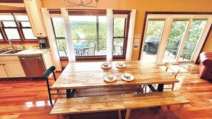 Un comedor con mesa y sillas de madera, una araña y ventanas amplias con vistas a follaje.
