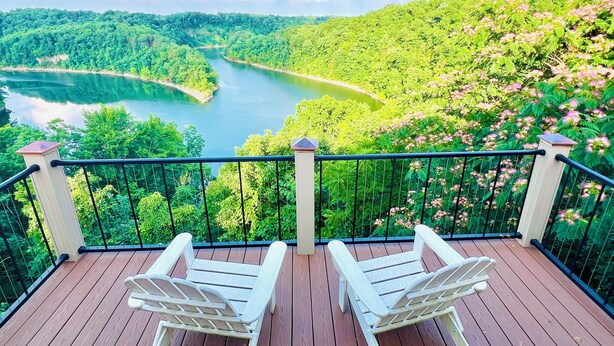 Terraza de madera con dos sillas blancas, con vistas a un río y colinas boscosas.
