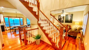 Un amplio espacio de sala con una escalera de madera, una mesa de comedor y un gran ventanal con vistas.