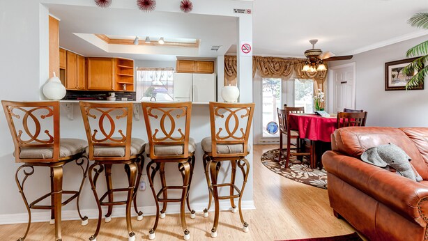 A dining area with four wooden chairs, a kitchen with wooden cabinets, and a living room with a leather sofa. - Palm Harbor Pool Home! 4bd~2ba - POOL home - SLEEPS 9! (Palm Harbor)