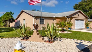 A building with a flagpole, a garage, and a landscaped front yard with plants and a fire hydrant. - Palm Harbor Pool Home! 4bd~2ba - POOL home - SLEEPS 9! (Palm Harbor)