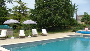 Une piscine entourée de verdure, avec des chaises longues blanches et des parasols.