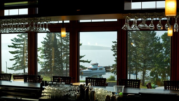 Un bar avec vue sur un lac et des bateaux, de grandes fenêtres et des luminaires suspendus.