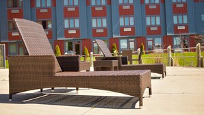 Des fauteuils de jardin en osier et une table sont placés devant un bâtiment dont les murs extérieurs sont peints en rouge et en bleu et qui possède de nombreuses fenêtres.