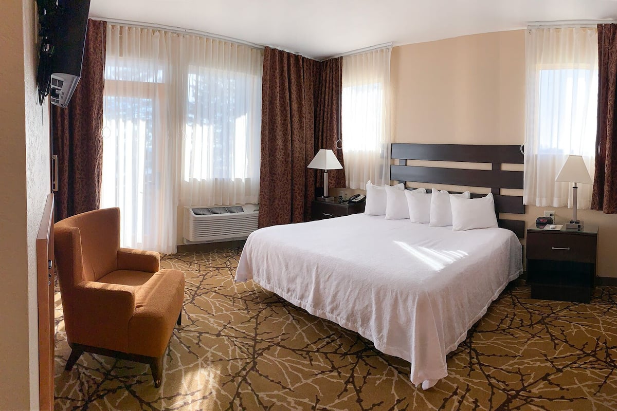 Een hotelkamer met een groot bed, een stoel, een nachtkastje en een raam met gordijnen.